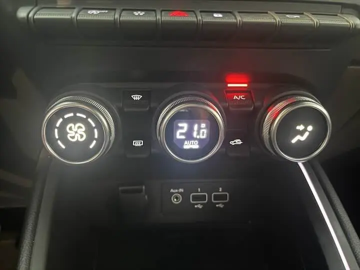 Gros plan sur les commandes de climatisation de la Renault Clio V blanche nacrée, affichant 21°C avec ventilateur actif.