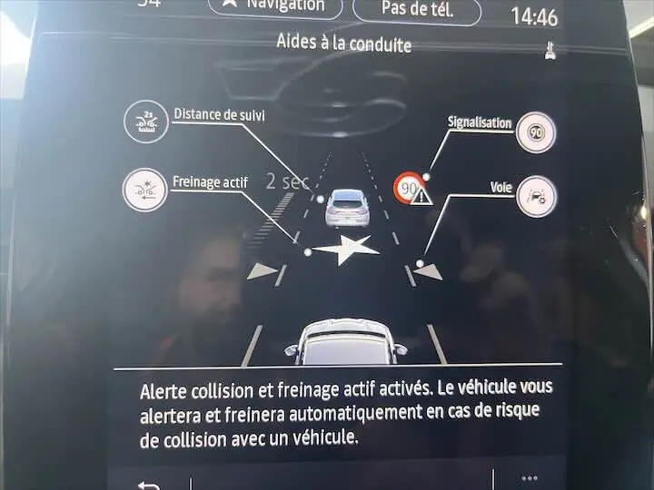 Affichage du système d'aide à la conduite sur écran, montrant une Renault Clio blanche vue de dessus avec alertes de freinage et signalisation.