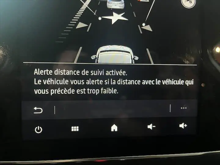 Affichage du tableau de bord de la Renault Clio V blanc nacré montrant l'alerte distance de suivi activée en vue avant du véhicule.