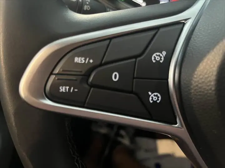 Gros plan sur les commandes de régulateur de vitesse au volant d'une Renault Clio V blanche nacrée de 2021.