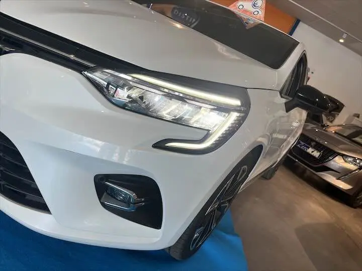 Vue 3/4 avant gauche d'une Renault Clio V blanche nacrée avec feux LED et jantes noires en concession.