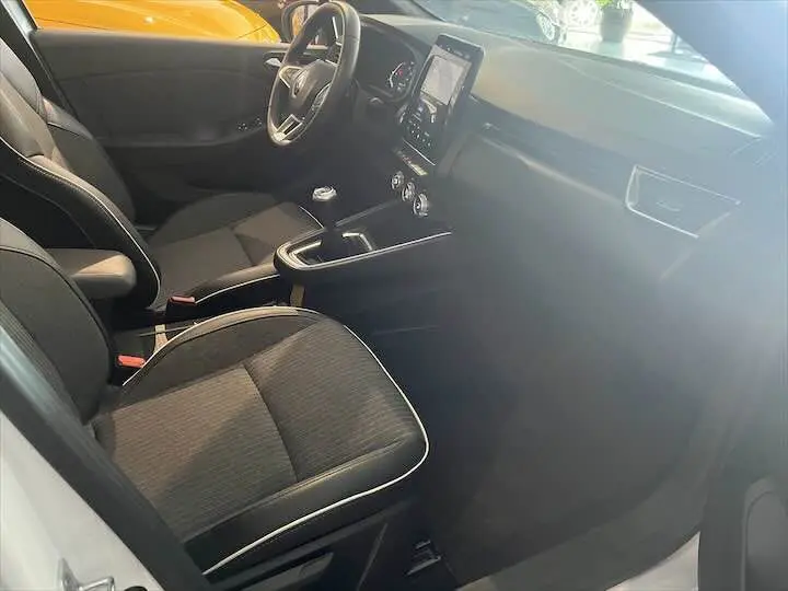 Vue intérieure côté conducteur de la Renault Clio V blanc nacré, avec sièges tissu noir et tableau de bord moderne.