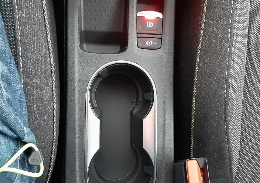Vue plongeante sur la console centrale noire du Renault Captur E-Tech Hybrid 2024, avec porte-gobelets et bouton frein à main électrique allumé.