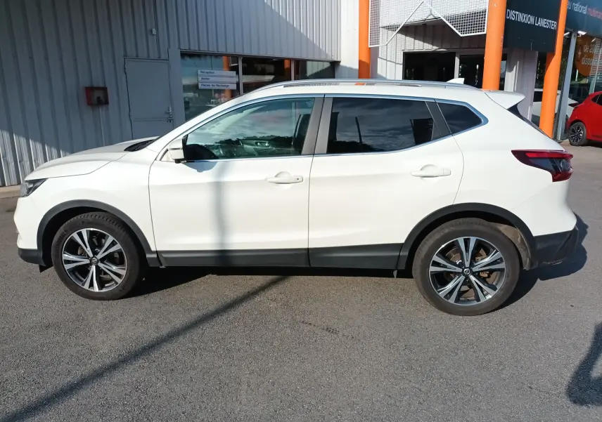 Profil côté gauche du Nissan Qashqai blanc nacré de 2019 avec jantes alliage bicolores et vitres teintées.