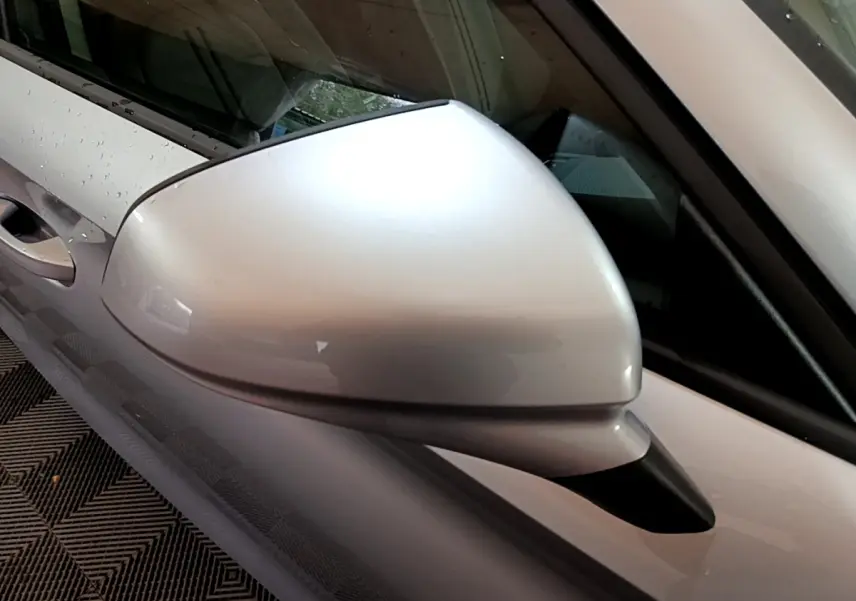 Rétroviseur côté gauche gris clair d'une SEAT LEON 2023, finition Business, avec carrosserie gris foncé visible en arrière-plan.