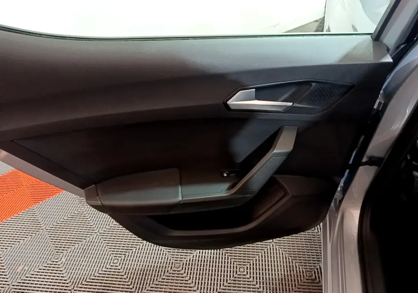 Vue rapprochée de la porte arrière droite gris foncé d'une SEAT LEON 2023 avec poignée argentée et accoudoir intégré.