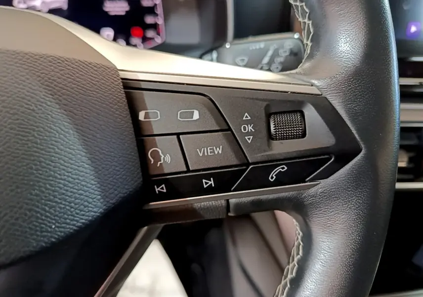 Gros plan sur les commandes au volant en cuir noir du SEAT Leon 2023, avec boutons multifonctions et molette tactile.