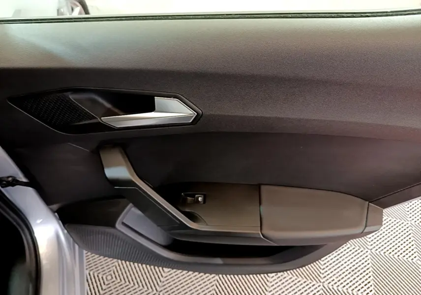 Gros plan sur la porte intérieure côté gauche d'une SEAT Leon gris foncé, avec poignée argentée et commande de vitre.