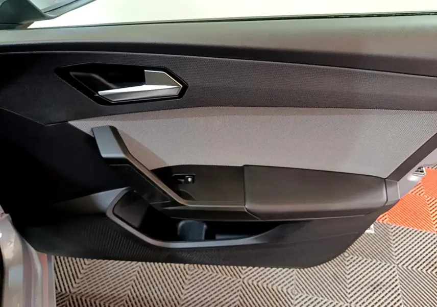 Intérieur côté gauche de la porte d'une SEAT LEON gris foncé, avec poignée argentée et panneau textile gris.