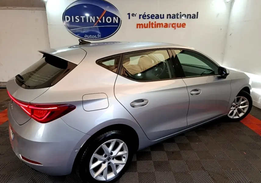 SEAT Leon gris clair vue 3/4 arrière droit dans un showroom avec feux arrière LED allumés.