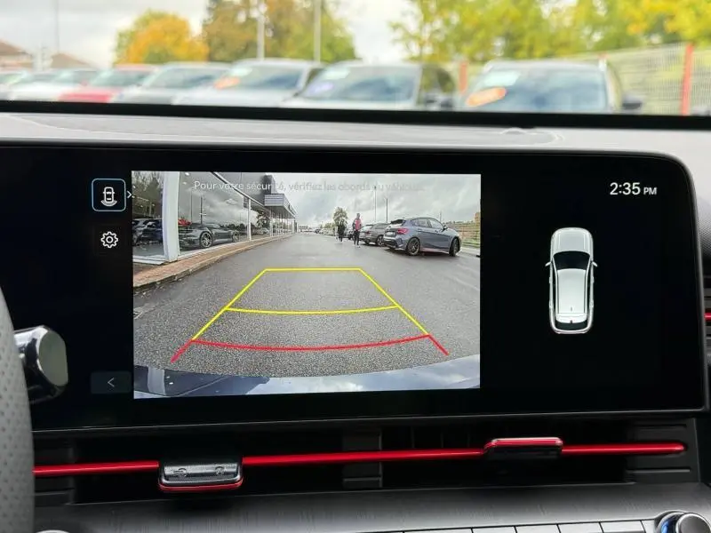 Vue arrière via caméra de recul du Hyundai Kona Cyber Gray métallisé, montrant la route et véhicules stationnés sur le côté droit.