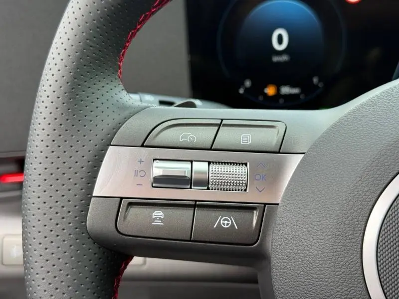 Gros plan sur les commandes multifonctions gauche du volant cuir perforé rouge du Hyundai Kona Cyber Gray 2025.