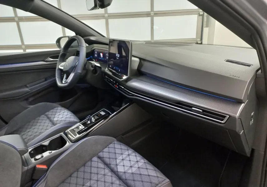 Vue intérieure côté conducteur de la Volkswagen Golf 2.0 TDI R-Line 2026 avec sièges gris à motifs et tableau de bord moderne.