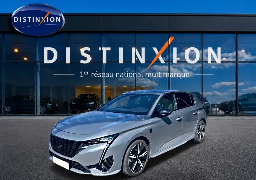 Peugeot 308 1.2 hybrid gris vue 3/4 avant droit, avec jantes alu et calandre noire distinctive.