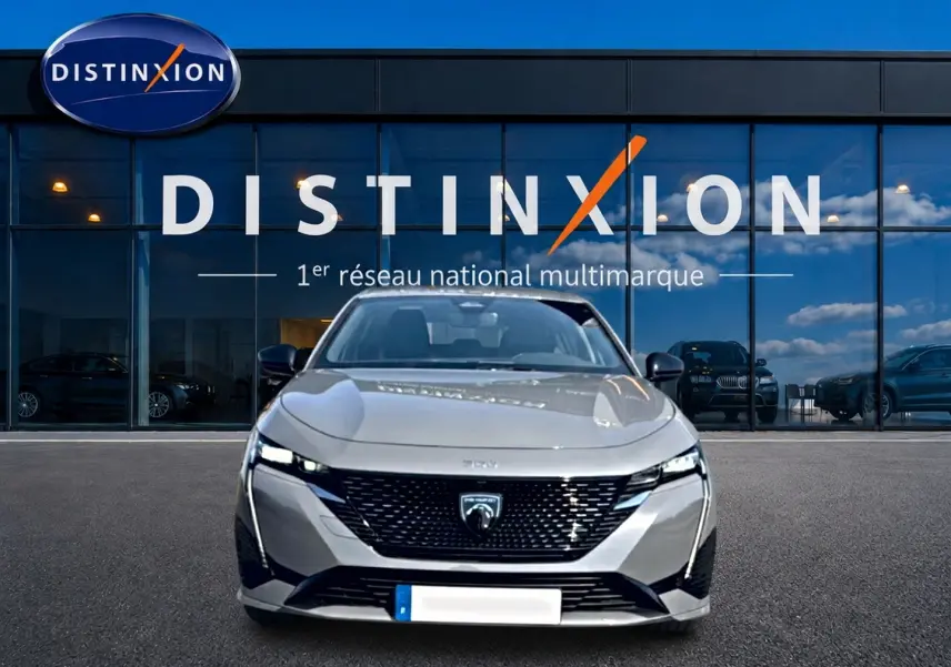 Vue avant d'une Peugeot 308 gris métallisé 2025 garée devant une vitrine avec logo Distinxion.