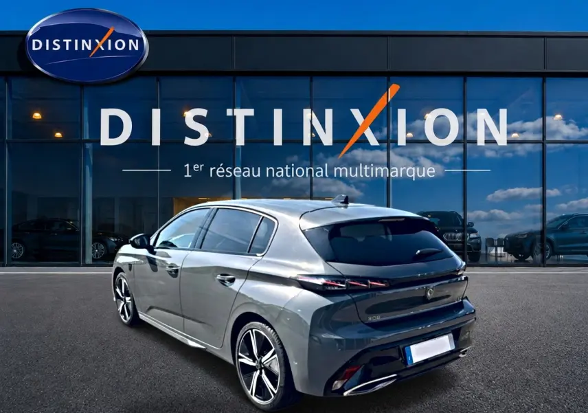 Peugeot 308 gris en 3/4 arrière droit, avec vitres surteintées et jantes alliage distinctives, devant une vitrine Distinxion.