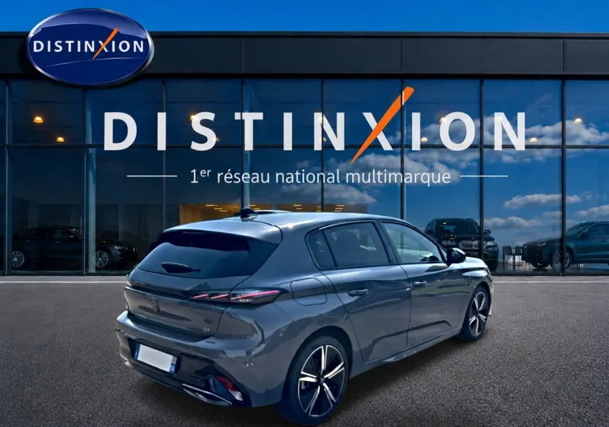 Vue 3/4 arrière droite d'une Peugeot 308 gris métallisé avec jantes alliage, devant une vitrine Distinxion.