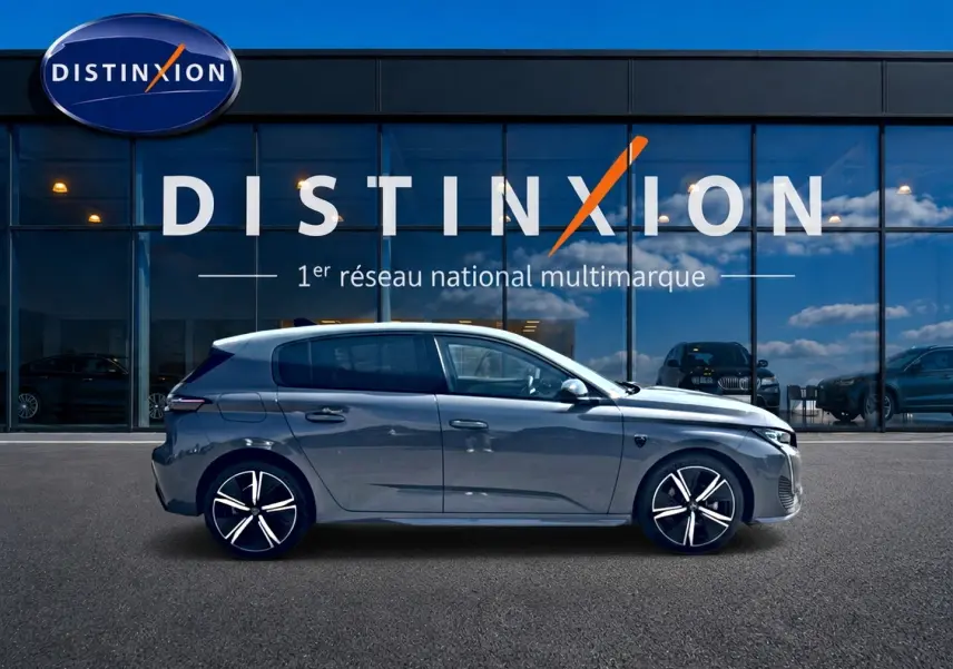 Peugeot 308 gris vue de profil côté gauche devant une vitrine avec logo Distinxion, jantes alu noires et argent.