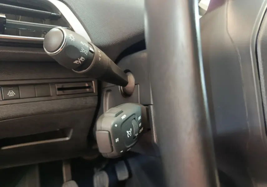 Gros plan sur les commandes au volant noir du Peugeot 3008 bleu, mettant en valeur le régulateur de vitesse et les phares automatiques.