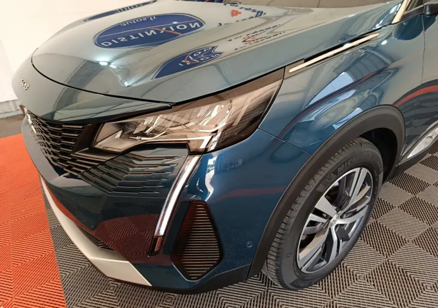 Vue 3/4 avant droit d'un Peugeot 3008 bleu avec phares LED et jante alliage visible sur sol en damier.