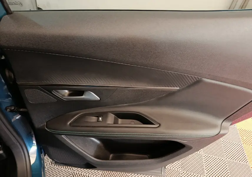 Vue rapprochée de la porte avant gauche du Peugeot 3008 bleu, avec garniture noire et surpiqûres vertes visibles.