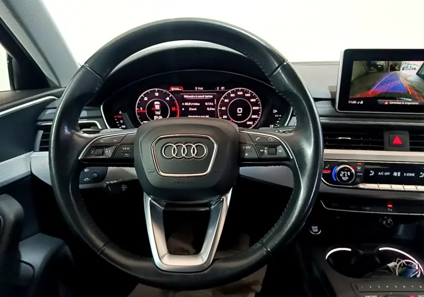Vue intérieure centrée sur le volant cuir noir d'Audi A4 40 TDI avec tableau de bord digital et écran multimédia arrière.