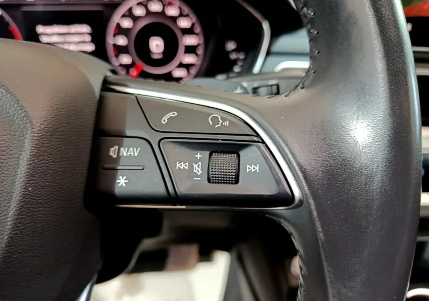 Gros plan sur les commandes gauche du volant cuir noir de l'Audi A4 40 TDI 2018 avec tableau de bord numérique en arrière-plan.