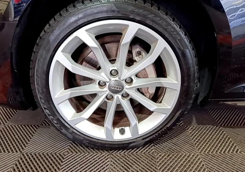 Gros plan sur la roue avant droite avec jante argentée de l'Audi A4 noire 40 TDI 2018 Design Luxe.