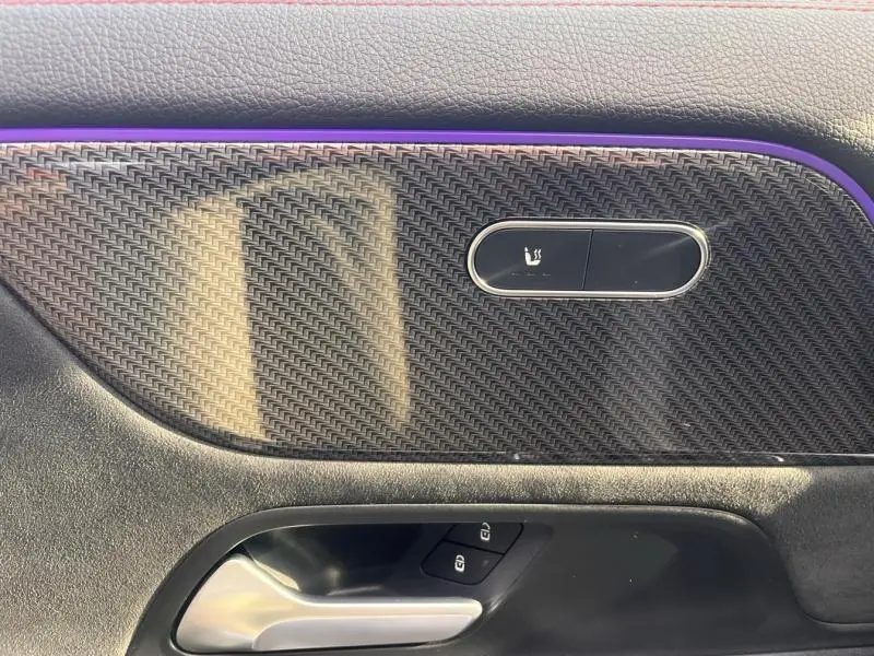 Détail de la garniture carbone et bouton de siège chauffant sur la porte côté gauche d’un Mercedes GLA 200 d AMG Line gris montagne.