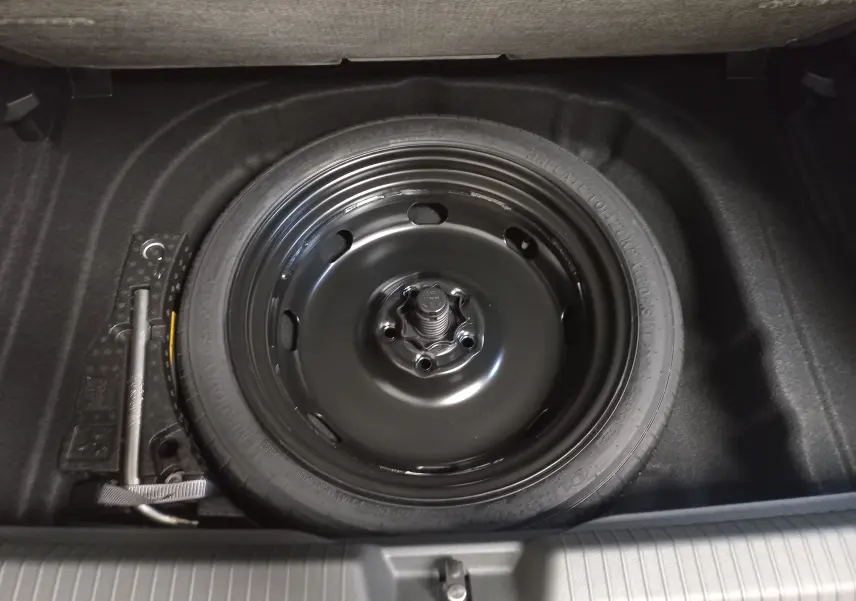 Vue plongeante sur la roue de secours compacte noire et le cric dans le coffre d'une Volkswagen Golf gris lunaire 2026.