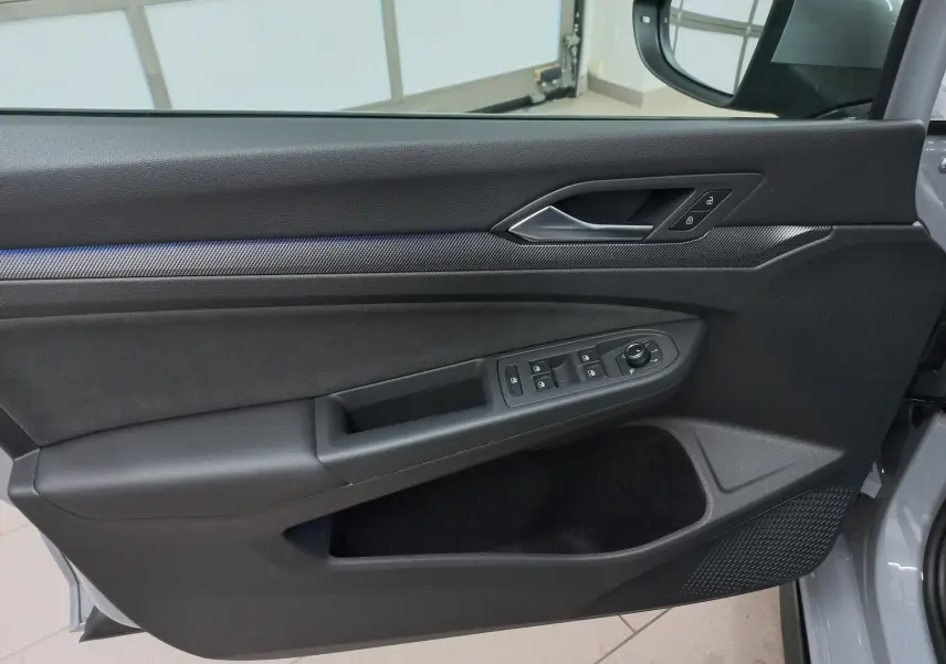 Vue intérieure côté gauche de la porte d'une Volkswagen Golf gris lunaire avec commandes électriques et insert carbone.