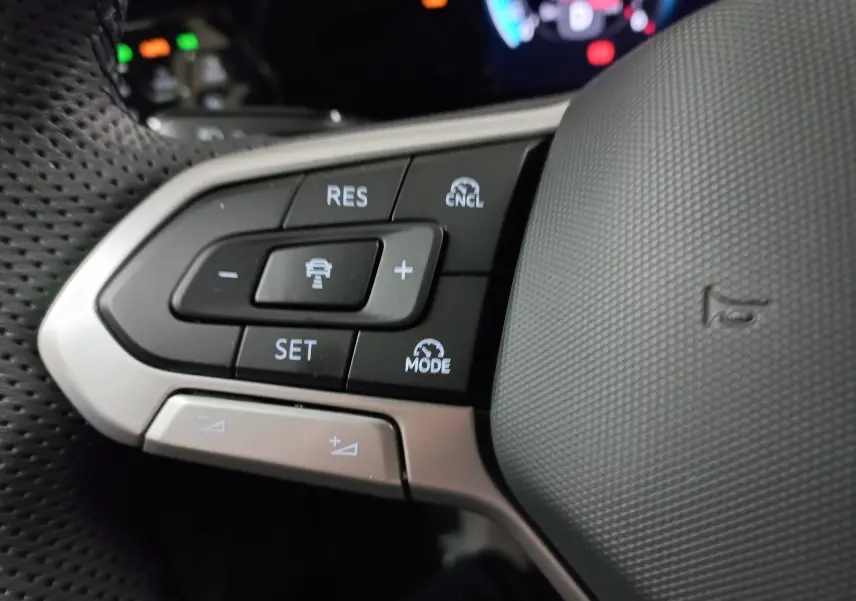 Gros plan sur les commandes au volant côté gauche du Volkswagen Golf gris lunaire avec fonctions de régulateur adaptatif.