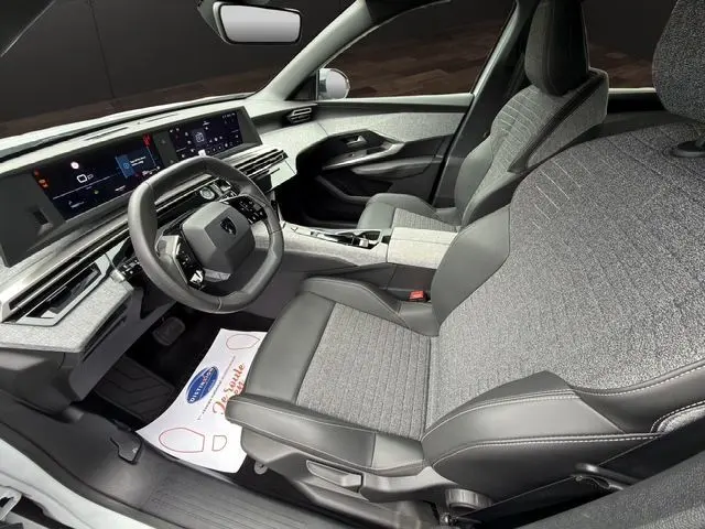 Vue intérieure côté conducteur du Peugeot 5008 Allure Hybrid 2025, mettant en valeur la sellerie tissu gris et le tableau de bord numérique panoramique.