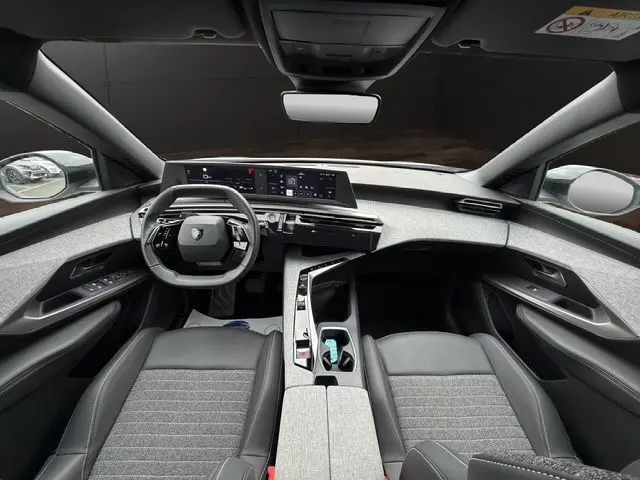 Vue intérieure avant du Peugeot 5008 Allure Hybrid 2025, tableau de bord moderne avec double écran et sellerie tissu gris.