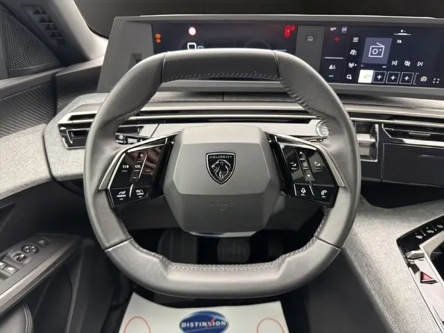 Vue rapprochée du volant compact en cuir noir du Peugeot 5008 Nouveau Allure Hybrid, avec tableau de bord numérique et finitions grises.