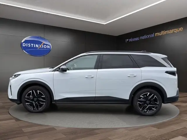 Vue latérale droite du Peugeot 5008 Nouveau Allure Hybrid blanc Okenite avec jantes alliage noires et toit noir dans un showroom.