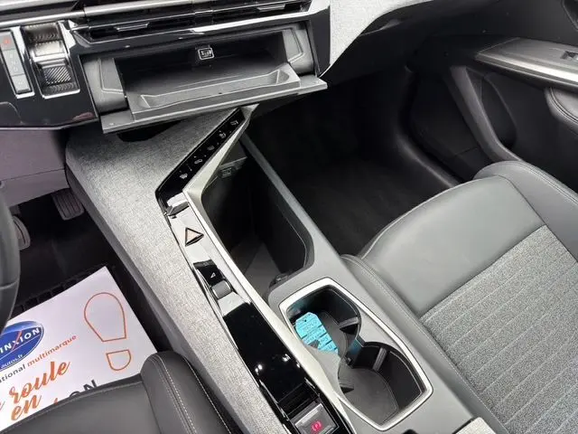 Vue intérieure du Peugeot 5008 Allure Hybrid blanc, montrant la console centrale avec rangement ouvert et sellerie tissu gris et cuir noir.