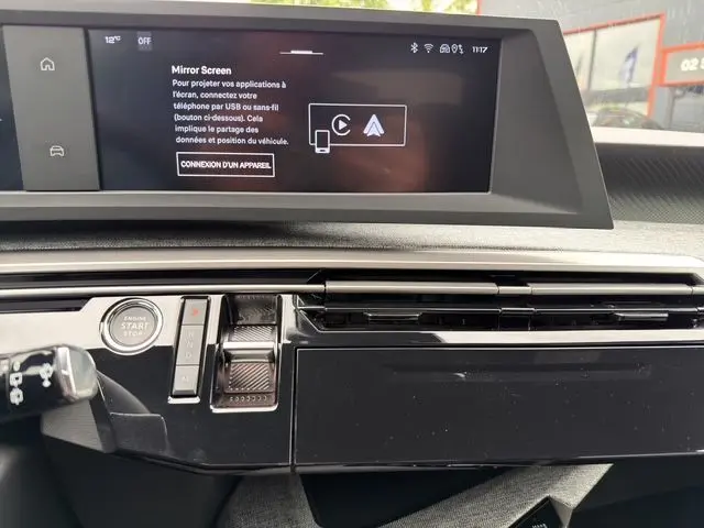 Gros plan sur l’écran tactile et la console centrale noire laquée du tableau de bord du Peugeot 5008 Allure Hybrid blanc.