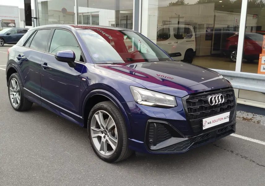 Audi Q2 bleu Navarre en 3/4 avant droit, avec calandre noire et jantes alliage bicolores visibles.