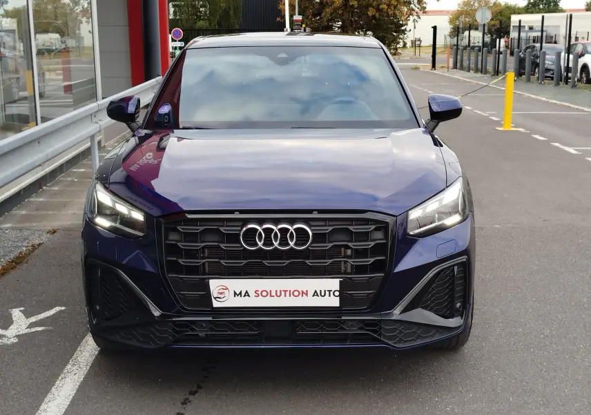 Vue de face d’un Audi Q2 35 TFSI S line bleu Navarre avec calandre noire et phares LED allumés.