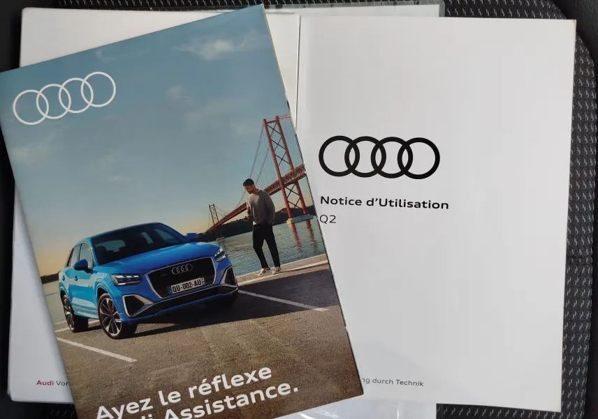 Vue 3/4 avant d'un Audi Q2 bleu Navarre garé près d'un pont rouge avec un homme debout à côté.