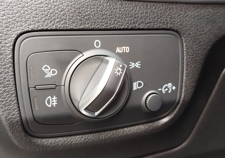 Gros plan sur le sélecteur de feux avec réglage automatique dans l’habitacle noir de l’Audi Q2 35 TFSI S line 2023.