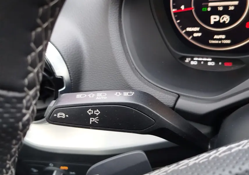 Gros plan sur le commodo gauche du volant d’un Audi Q2 35 TFSI 2023, avec tableau de bord numérique en arrière-plan.