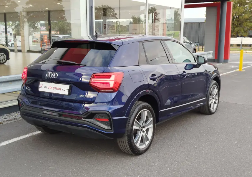 Audi Q2 bleu Navarre vue 3/4 arrière droit, avec feux LED et jantes alliage 18 pouces bicolores.