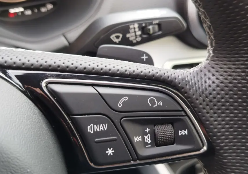 Gros plan sur les commandes multifonctions du volant en cuir perforé d'un Audi Q2 35 TFSI 2023, finition S line.