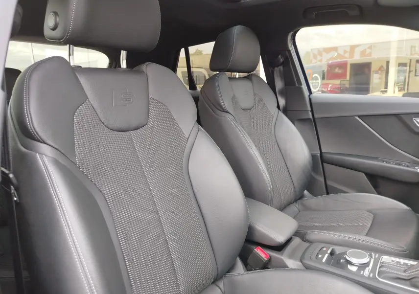 Vue intérieure de l'Audi Q2 2023, sièges avant en cuir noir avec logo S embossé et toit ouvrant panoramique.