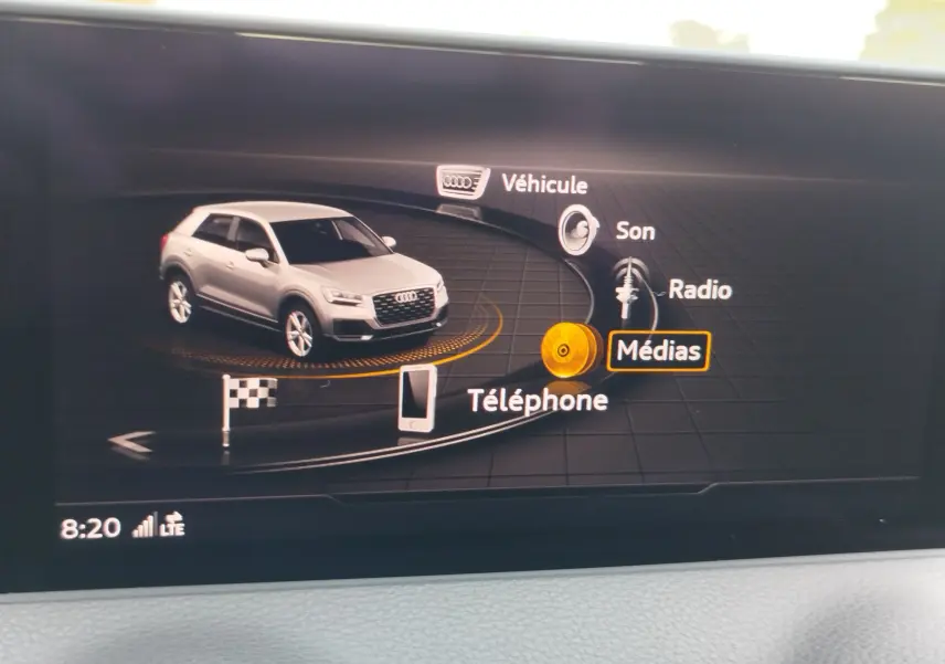 Affichage numérique intérieur montrant une Audi Q2 blanche en 3/4 avant dans le menu multimédia du véhicule.