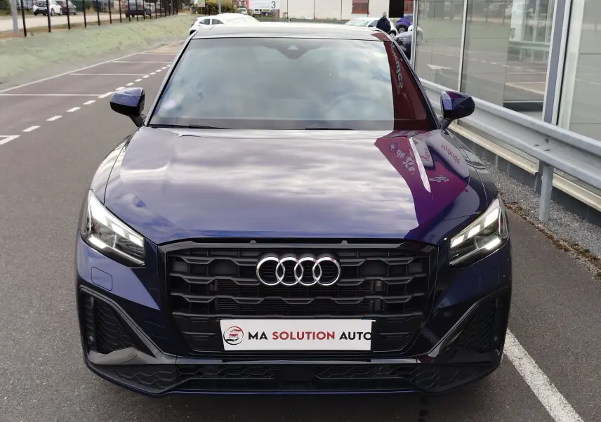 Vue avant d'un Audi Q2 35 TFSI S line bleu Navarre avec calandre noire et feux LED allumés.