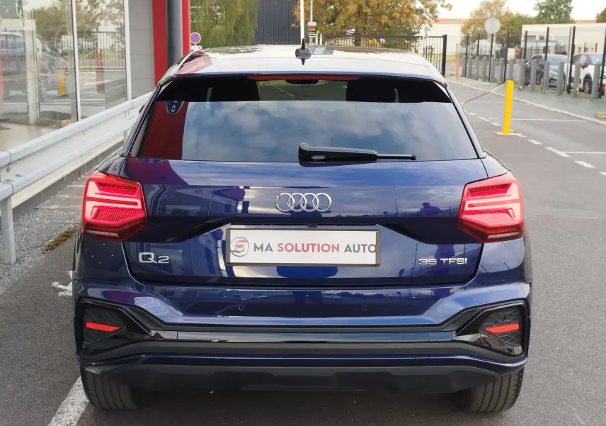 Vue arrière d'un Audi Q2 bleu Navarre 2023 avec feux LED allumés et logo 35 TFSI visible sur le hayon.