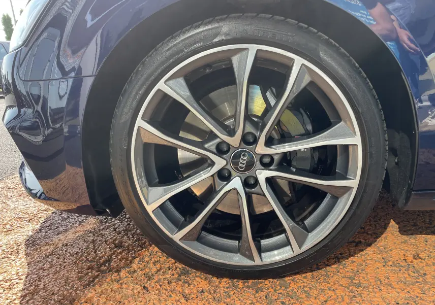 Gros plan sur la roue avant gauche d'une Audi S4 bleu Navarre, mettant en valeur la jante alliage à multiples branches.